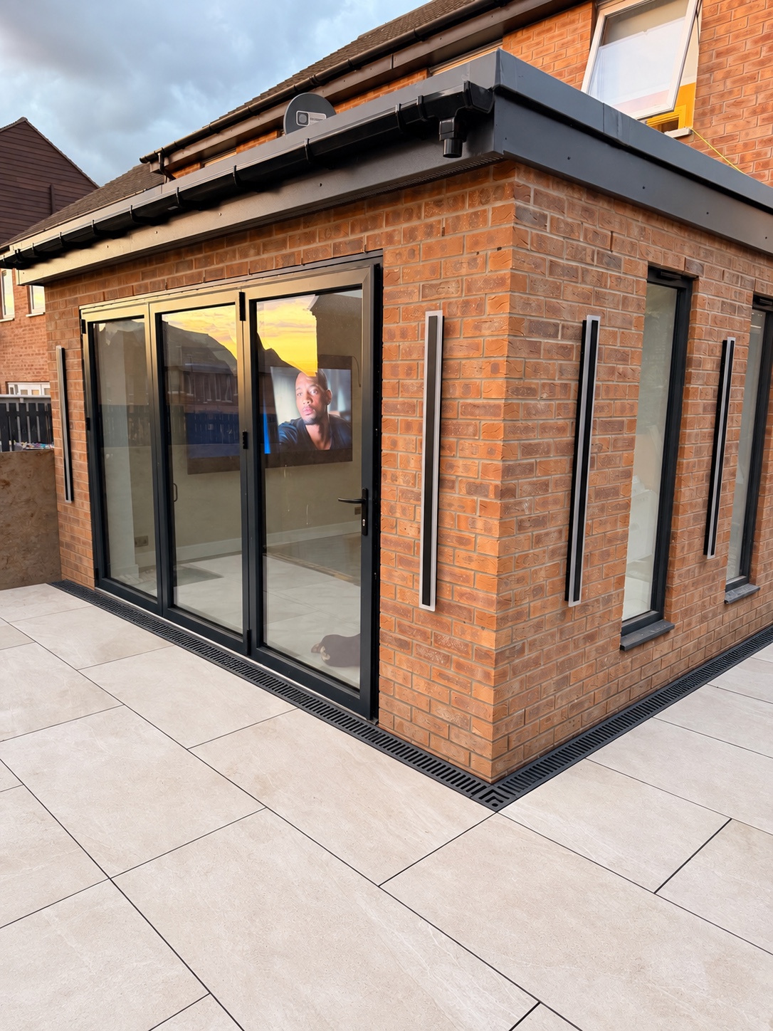 Completed contemporary brick rear extension with black aluminium bifold doors, flat roof and porcelain patio